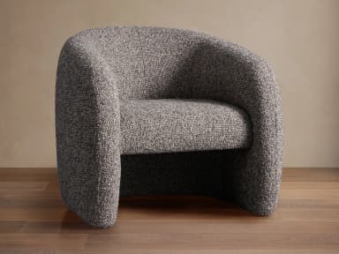A generously proportioned armchair with a rounded, enveloping silhouette. The chair features a fully upholstered form with a high back that curves around to form integrated armrests. The upholstery has a textured, boucle-like appearance, creating a soft and inviting aesthetic. The base appears to be a continuous, rounded structure that extends to the floor, without visible legs. — 3D model