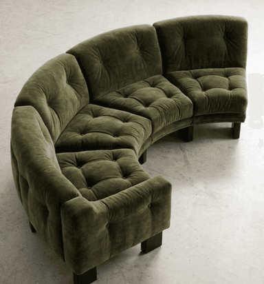 A large, modular curved sectional sofa upholstered in a plush olive green velvet fabric. The sofa is composed of multiple individual seating units that connect to form a sweeping curve. Both the seat cushions and the backrests feature deep button tufting, contributing to a soft, inviting aesthetic. The sofa rests on discreet, short, dark-colored block legs. — 3D model