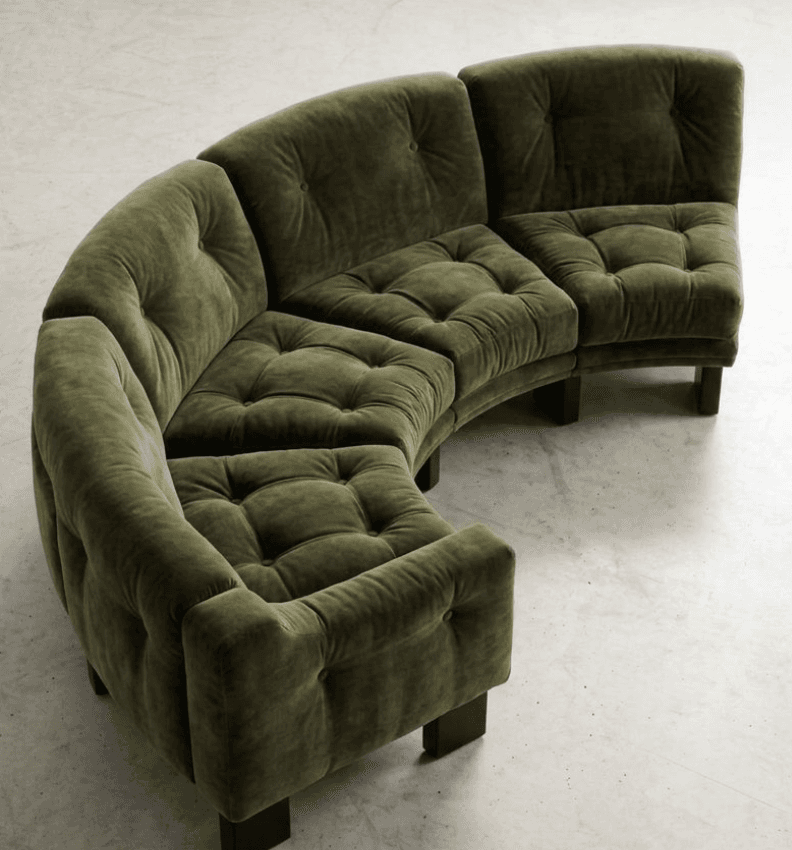 A large, modular curved sectional sofa upholstered in a plush olive green velvet fabric. The sofa is composed of multiple individual seating units that connect to form a sweeping curve. Both the seat cushions and the backrests feature deep button tufting, contributing to a soft, inviting aesthetic. The sofa rests on discreet, short, dark-colored block legs. — 3D model