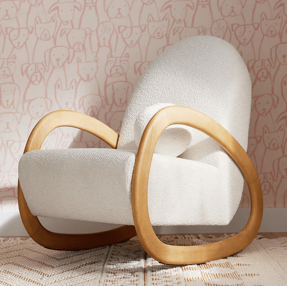 A contemporary rocking chair featuring a plush, off-white boucle upholstered seat and back, supported by a distinctive curved light wood frame that also forms the armrests and rocking base. The design emphasizes organic shapes and a seamless integration of materials. — 3D model