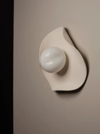 A modern sculptural wall sconce featuring an organic, leaf-like cream-colored backplate made of ceramic or plaster, paired with a spherical frosted glass diffuser. The design is minimalist and fluid, providing soft, diffused illumination. — 3D model