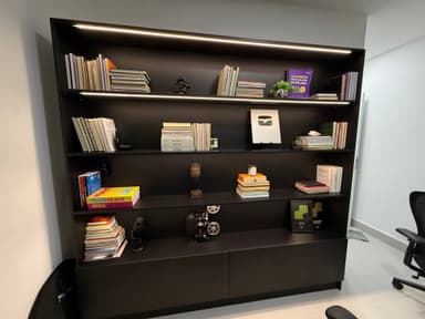 A tall, modern bookshelf featuring multiple open shelves for display and two closed storage cabinets at the base. The unit is finished in a matte black color and is filled with various books and decorative items. — 3D model