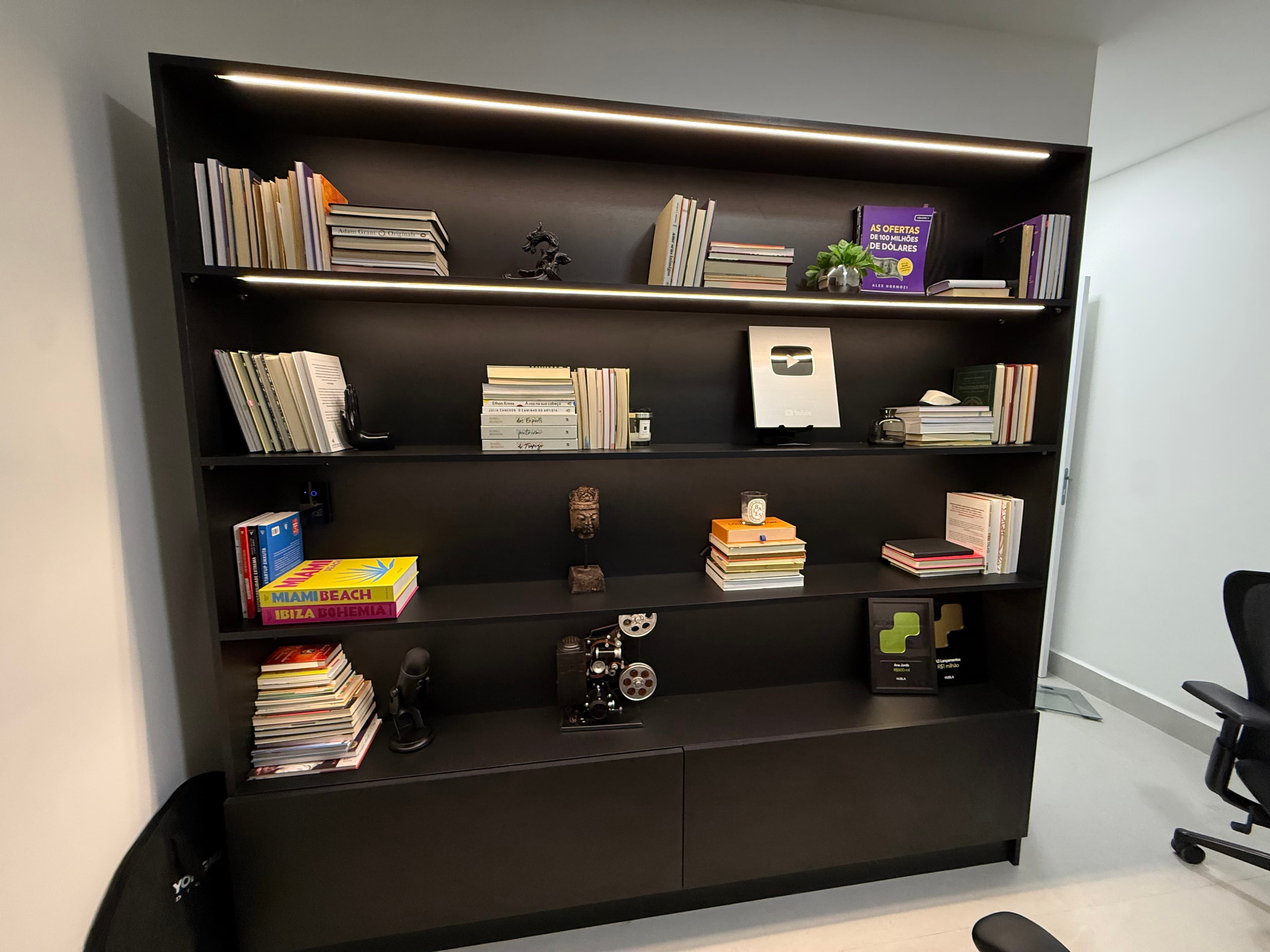 A tall, modern bookshelf featuring multiple open shelves for display and two closed storage cabinets at the base. The unit is finished in a matte black color and is filled with various books and decorative items. — 3D model