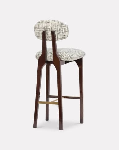 A high-backed bar stool featuring a dark stained wooden frame, a contoured upholstered seat, and a separate, floating upholstered backrest. The frame includes splayed legs and a brass footrest. The upholstery is a textured, patterned fabric in monochrome tones. — 3D model