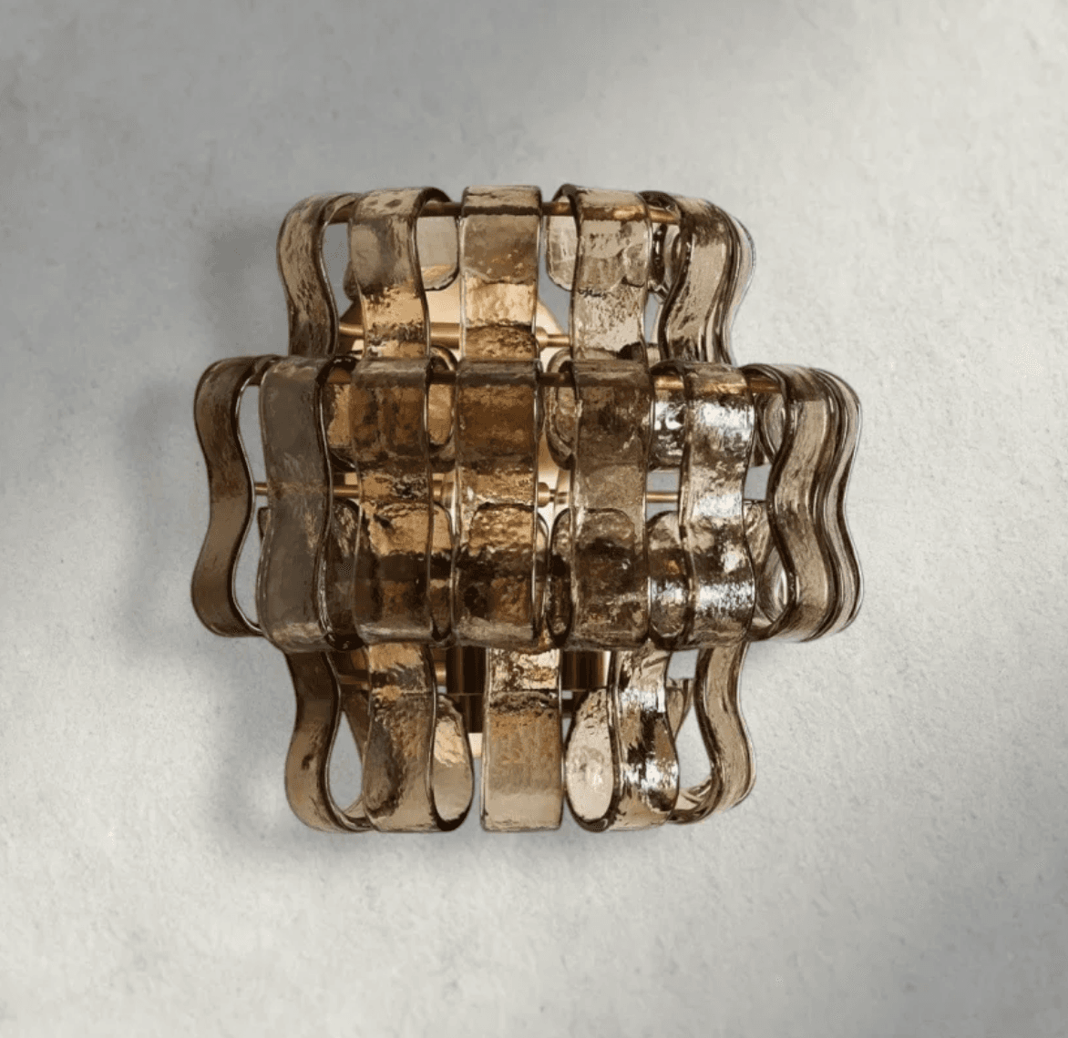 A contemporary wall sconce featuring multiple horizontal bands of textured, smoked or amber-toned glass, arranged in a layered, undulating pattern. The glass panels are secured by an underlying metallic frame, likely brass-finished, which is partially visible between the glass sections. The fixture is designed for vertical mounting and provides diffused, warm illumination. — 3D model