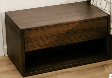 A compact, rectangular nightstand crafted from dark stained wood, featuring a single, handle-less drawer at the top and an open storage shelf beneath it. The wood displays a prominent grain texture, and the overall design is minimalist and contemporary. — 3D model