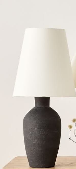 A modern table lamp featuring a conical fabric shade in an off-white color, paired with a tapered, vase-shaped base in matte black with a distinctive textured finish. The lamp exhibits a minimalist aesthetic. — 3D model