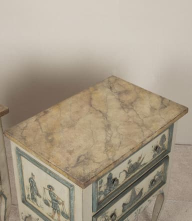 A pair of matching nightstands with two drawers each. The front panels of the drawers and the lower skirt are adorned with hand-painted blue and white scenic details, featuring boats and architectural elements. The nightstands have a distressed cream-colored finish and are supported by four cabriole legs. The top surface appears to be a different material, possibly a veneer or stone. — 3D model