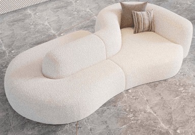 A modular, organic-shaped sofa with a textured boucle fabric upholstery. The sofa features a distinctive curved design with distinct seating sections and an integrated armrest/backrest element. Two decorative throw pillows are placed on the seating area, one solid taupe and the other with a striped pattern. — 3D model