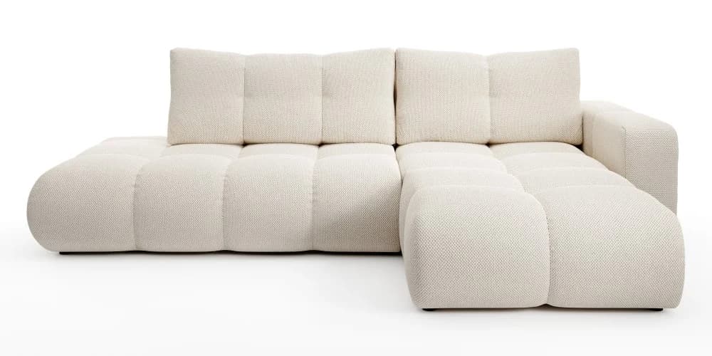 A modular sectional sofa with a low profile and plush cushioning. The sofa features tufted seating and backrest surfaces, creating a segmented visual appearance. It is upholstered in a textured cream-colored fabric and has a rounded chaise lounge extension on the left side. — 3D model