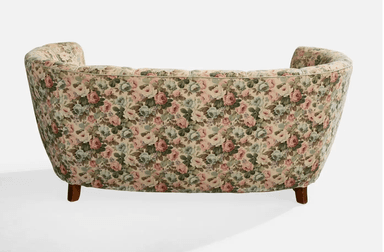 A vintage-style, curved sofa upholstered in a floral fabric with a pastel color palette. The sofa features a rounded backrest with vertical channeling and integrated armrests that curve inwards. It is supported by four short, tapered wooden legs. — 3D model