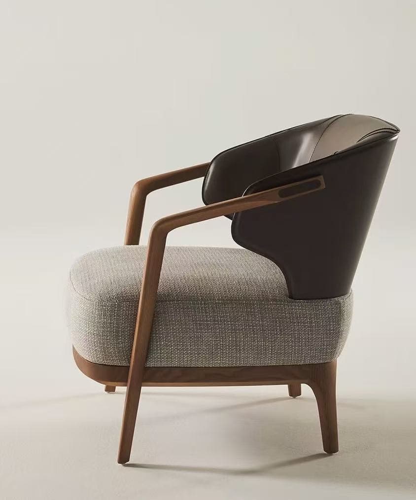 A modern armchair featuring an exposed wooden frame, a generously upholstered seat in a light gray fabric, and a distinct backrest and armrest shell crafted from dark brown leather. The chair has a sleek profile with tapered legs and curved wooden armrests. — 3D model