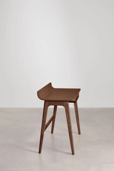 A minimalist wooden desk featuring a distinctive curved back panel and an integrated storage slot beneath the tabletop. The desk stands on four tapered, angled legs connected by a horizontal stretcher. — 3D model
