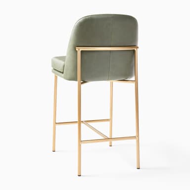 A contemporary bar stool featuring a comfortable green faux leather upholstered seat and backrest, supported by a slim, gold-finished metal frame with an integrated footrest. — 3D model