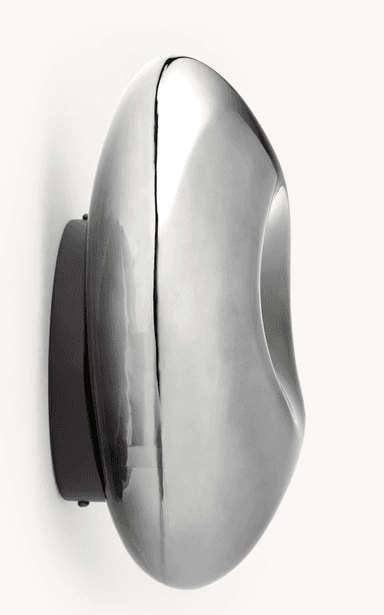 A modern wall-mounted light fixture featuring a fluid, organic, and irregularly shaped front in a highly polished chrome or metallic finish. It is mounted on a flat, dark backplate, contrasting with the reflective, undulating surface of the main light element. The design is sculptural and abstract, intended to provide ambient light while serving as a decorative art piece. — 3D model