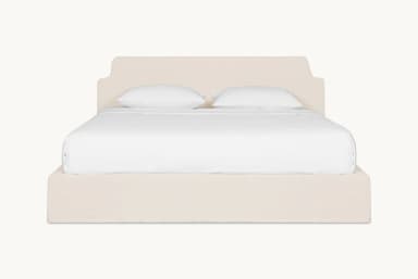 A bed frame with a padded headboard and platform base, covered in a neutral-toned fabric. The headboard has a distinctive silhouette with curved upper corners. The bed is shown with white linens and two pillows. — 3D model