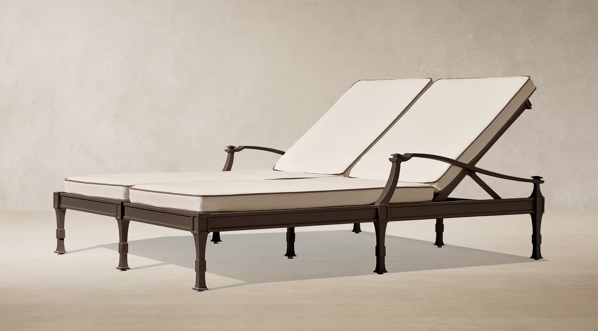 An outdoor adjustable double chaise lounge featuring a dark brown metal frame and two cream-colored cushioned sections with brown piping. Each section has an independently adjustable backrest and fixed armrests. The frame exhibits decorative casting on the legs and arm supports. — 3D model