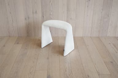 A white, textured stool with a unique U-shaped base. The stool appears to be upholstered in a boucle or teddy bear fabric. Its curved structure provides a modern and organic aesthetic. — 3D model