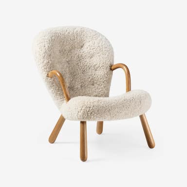 A contemporary lounge chair featuring a fully upholstered body in cream shearling fabric, with integrated curved wooden armrests and splayed wooden legs. — 3D model