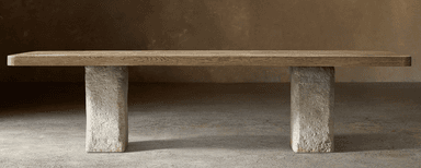 A rectangular coffee table featuring a thick, light-toned wood plank top with visible grain, supported by two substantial, roughly textured stone or concrete block legs. The design emphasizes natural materials and a minimalist, robust aesthetic. — 3D model