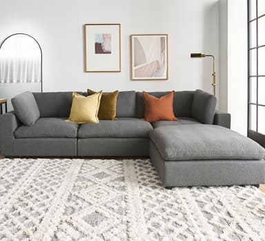 A contemporary gray fabric sectional sofa featuring a modular design, an L-shaped configuration, and a chaise lounge extension. It includes loose back cushions and is accessorized with several accent pillows in warm tones. — 3D model