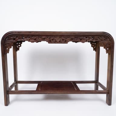 A long, narrow dark brown wooden console table featuring a rectangular top with gently curved ends and an intricately carved apron. It is supported by four straight legs and includes a lower recessed shelf. — 3D model