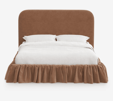 A fully upholstered bed frame featuring a soft brown/taupe fabric, a generously padded headboard with smoothly rounded corners, and a matching ruffled bed skirt that conceals the frame. The bed is presented with clean white bedding, including a duvet and two pillows, creating a plush and inviting appearance. The design emphasizes comfort and a cohesive, soft aesthetic. — 3D model