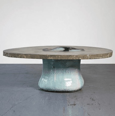 A low, circular accent table featuring a concrete top and a ceramic base. The rough-textured concrete top incorporates a central, irregularly shaped inlay of glazed ceramic in shades of blue and white. The base is a bulbous, hand-glazed ceramic form with a light blue/aqua finish, showing organic variations and a subtly textured surface. The overall design suggests an artisanal, wabi-sabi aesthetic. — 3D model