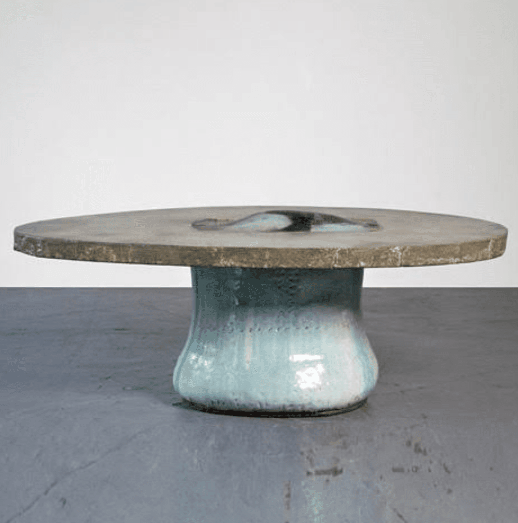 A low, circular accent table featuring a concrete top and a ceramic base. The rough-textured concrete top incorporates a central, irregularly shaped inlay of glazed ceramic in shades of blue and white. The base is a bulbous, hand-glazed ceramic form with a light blue/aqua finish, showing organic variations and a subtly textured surface. The overall design suggests an artisanal, wabi-sabi aesthetic. — 3D model