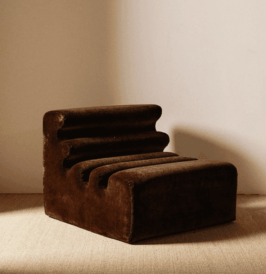 A low-profile, armless lounge chair upholstered in dark brown velvet or similar plush fabric, featuring a distinctive ribbed design on its backrest and seat. The chair has a sculptural, block-like form, with horizontal ridges creating a wave-like contour. It appears new and designed for comfort and aesthetic appeal in a contemporary setting. — 3D model