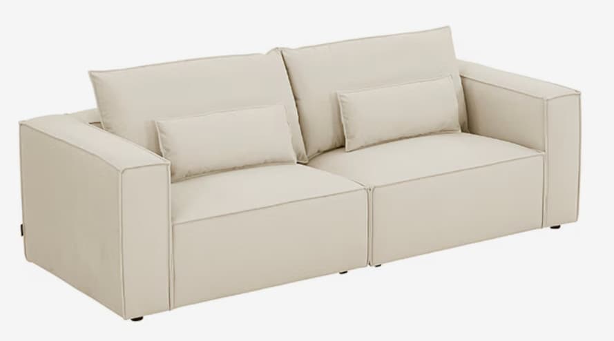 A modern two-seater sofa, presented in a studio shot, featuring a modular design. It is upholstered in a light, off-white fabric and composed of two distinct sections. Each section includes a deep seat cushion, a large rectangular back cushion, and a smaller accent pillow, all with visible piping detail. The arms are square and low-profile, contributing to a clean, contemporary aesthetic. — 3D model