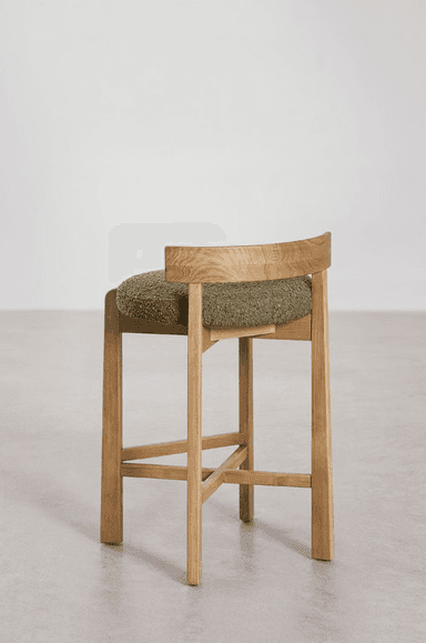 A modern counter stool crafted from light-toned oak wood, featuring a sturdy four-legged base with cross-stretchers for stability. The seat is a rounded, thick cushion upholstered in a textured, olive green bouclé fabric. A low, curved backrest is integrated into the rear legs, complementing the stool's contemporary design. — 3D model