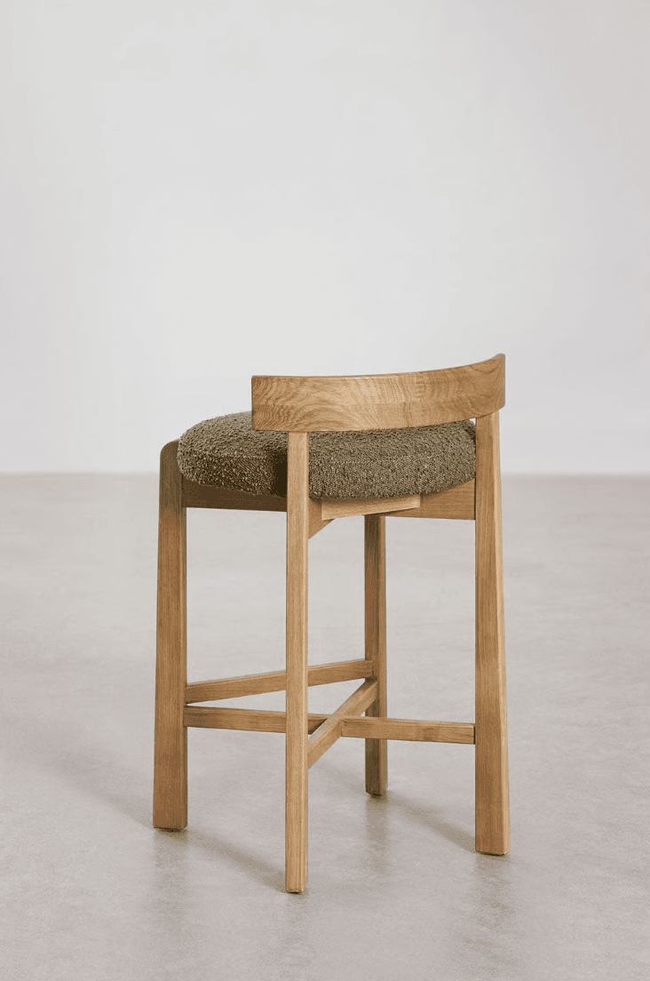 A modern counter stool crafted from light-toned oak wood, featuring a sturdy four-legged base with cross-stretchers for stability. The seat is a rounded, thick cushion upholstered in a textured, olive green bouclé fabric. A low, curved backrest is integrated into the rear legs, complementing the stool's contemporary design. — 3D model