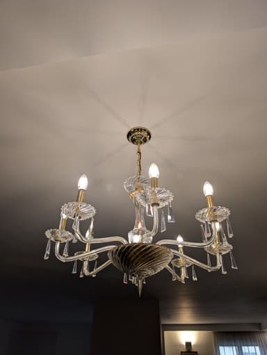 A multi-tiered chandelier with eight arms, featuring clear glass elements and crystal pendants. The central body has a twisted glass design, and the arms are curved, supporting candle-style light bulbs. The hardware appears to be gold-toned. — 3D model