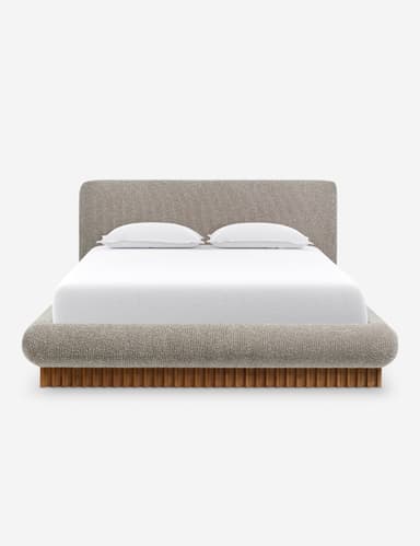 A side profile view of a modern upholstered bed with a curved headboard and a wooden slatted base. The bed frame is upholstered in a textured, light-colored fabric, and it features rounded edges. A white mattress with white bedding and a single white pillow are visible on top. — 3D model