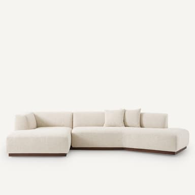 A sectional sofa with a low profile and upholstered in a textured, off-white fabric. It features a chaise lounge section on the left and a curved configuration. The sofa is supported by a dark wooden base. — 3D model