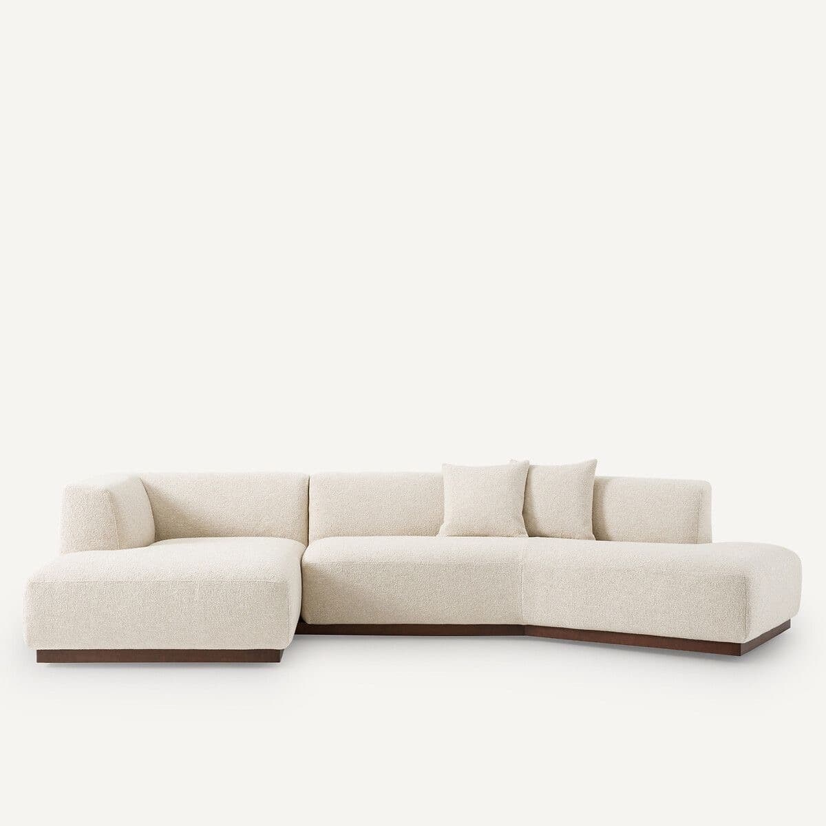 A sectional sofa with a low profile and upholstered in a textured, off-white fabric. It features a chaise lounge section on the left and a curved configuration. The sofa is supported by a dark wooden base. — 3D model