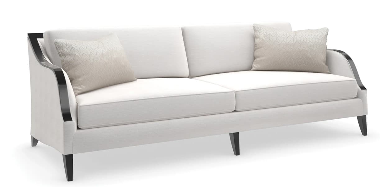 A contemporary sofa featuring light-colored upholstery, exposed dark wood arms with a curved design, and tapered dark wood legs. It has a two-over-two cushion configuration with subtle piping and is accompanied by two patterned accent pillows. — 3D model