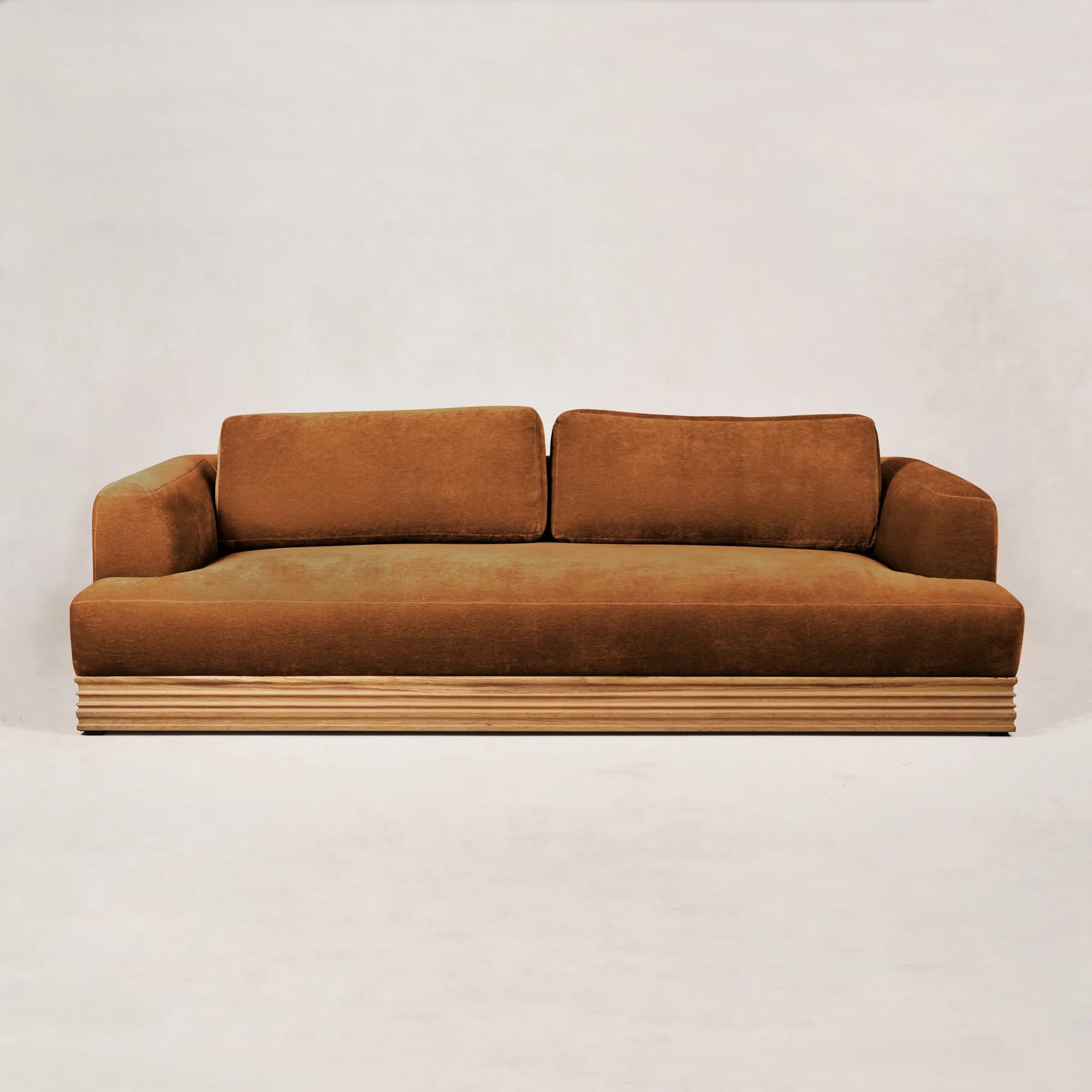 A modern three-seater sofa with plush, tufted cushions and a low profile. The sofa features a distinct wooden base with horizontal fluting, providing a contrasting texture and style to the upholstered body. The arms are integrated and curve gently upwards. — 3D model