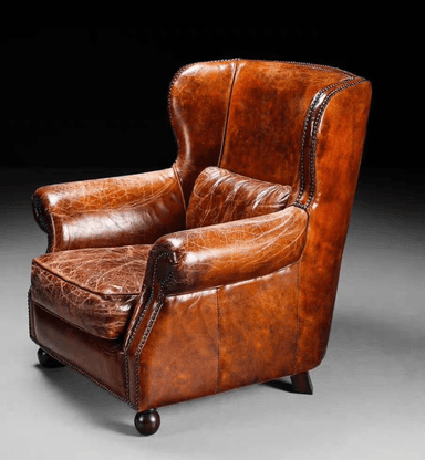 A traditional wingback armchair upholstered in rich, distressed brown leather, featuring prominent wingback sides, rolled arms, and extensive nailhead trim. It includes a loose seat cushion and a loose back cushion, supported by dark turned wooden bun feet. — 3D model