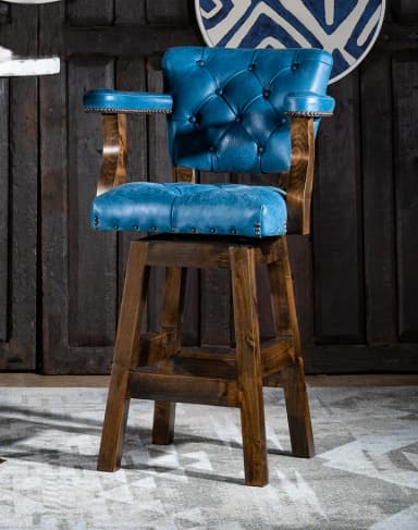 A traditional-style bar stool featuring a tufted, blue upholstered seat and back with armrests, supported by a dark wood frame. The seat includes a swivel mechanism and is adorned with decorative nailhead trim. The sturdy wooden base has a footrest. — 3D model