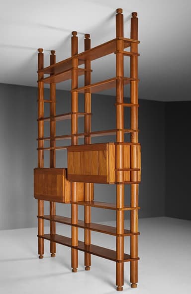 A tall, free-standing shelving system crafted from teak wood, featuring multiple open shelves and two integrated closed cabinet modules. The structure is defined by cylindrical vertical posts with turned finial details at the top and bottom, which support adjustable or fixed horizontal shelves. The cabinet fronts feature vertical slatted panels, contributing to its mid-century Italian aesthetic. — 3D model