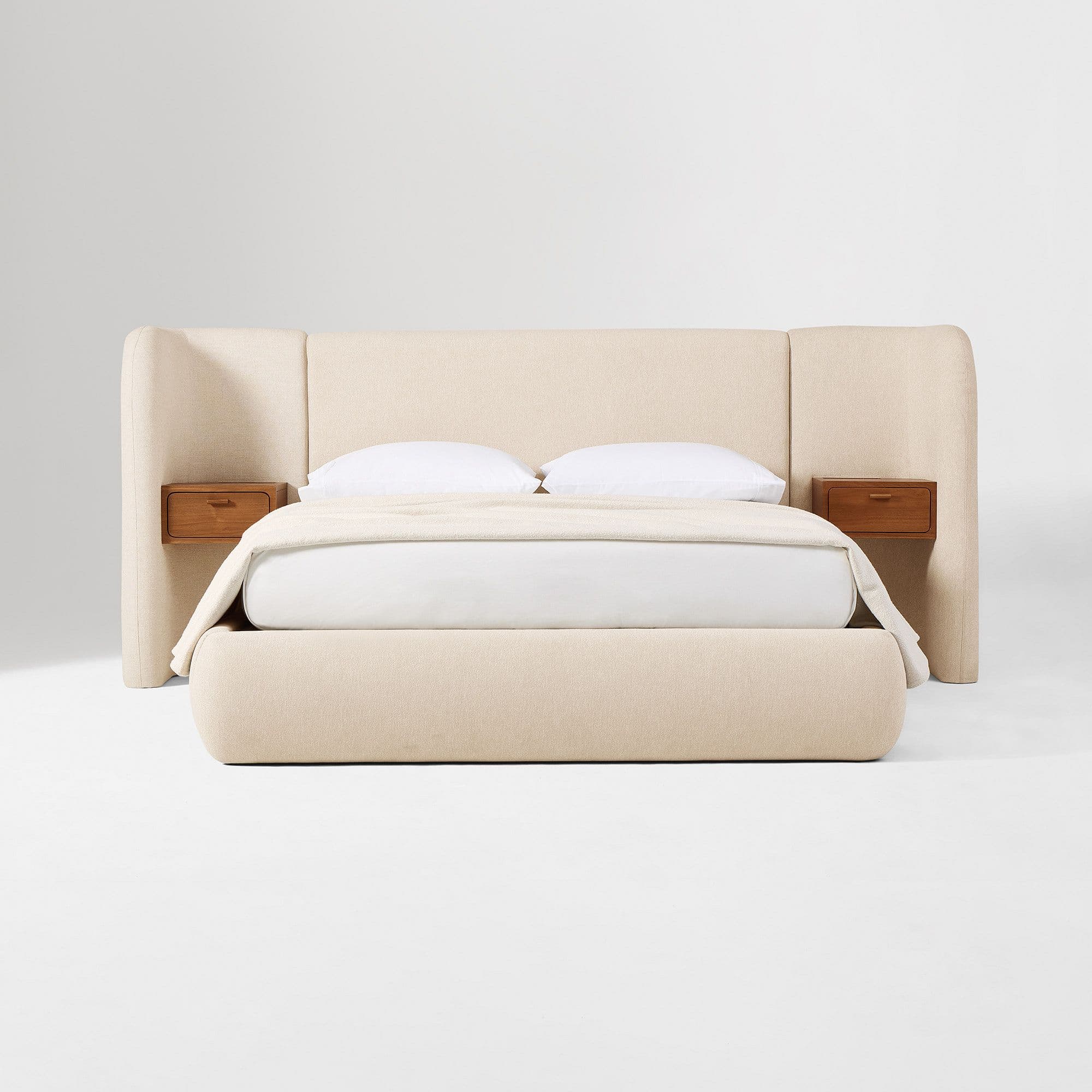 A platform bed with an integrated upholstered headboard that extends to the sides, creating wing-like panels. Two small, wooden nightstands are mounted on the wing panels, one on each side. The bed frame and headboard are upholstered in a textured, light-colored fabric. The mattress is covered with white linens and a light beige throw blanket. — 3D model