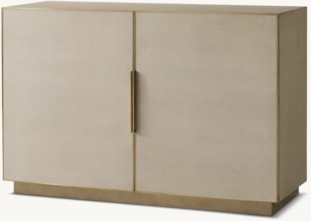 A rectangular two-door sideboard featuring a light beige, textured faux shagreen finish. The cabinet is accented with thin brass trim around the top edge, side panels, and vertically between the doors. It includes two integrated, vertical brass pull handles on the doors. The entire unit rests on a recessed plinth-style brass base, giving it a floating appearance. — 3D model