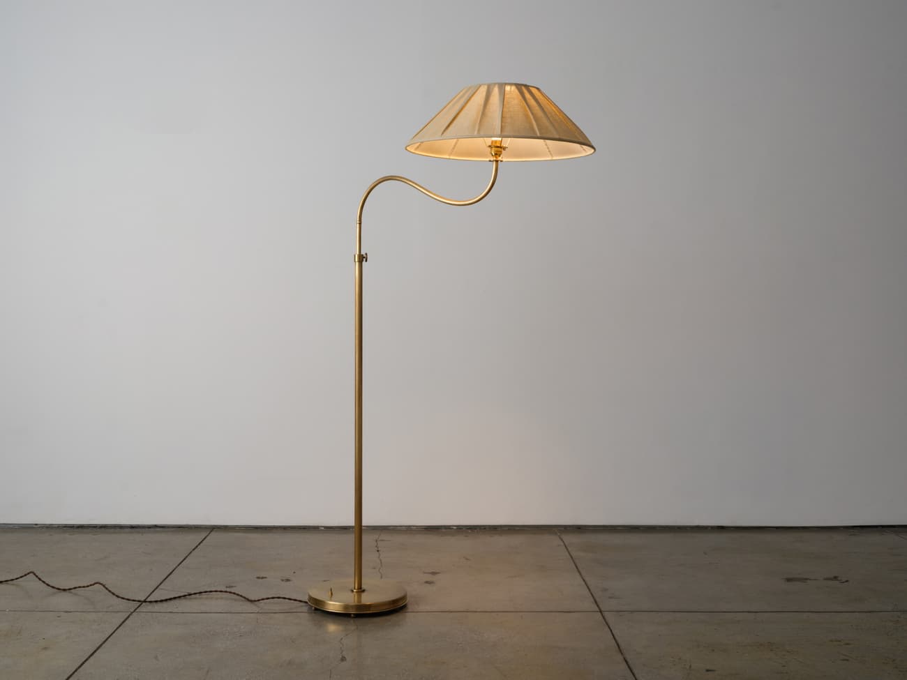 A brass-finished swing-arm floor lamp featuring a circular base, a slender vertical stem, and an articulated arm that supports a conical, pleated fabric lampshade. The lamp appears to be in new or excellent condition. — 3D model