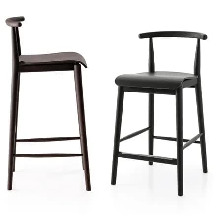 A contemporary bar stool featuring a dark stained wooden construction, including a round seat, four splayed legs, and a low curved backrest that subtly integrates into armrests. A horizontal metal bar serves as a footrest on the front. — 3D model