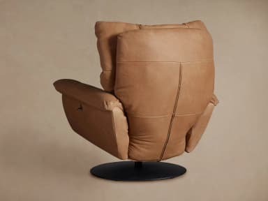 A contemporary armchair upholstered in tan leather, featuring a plush, segmented backrest and seat, rounded armrests, and a circular swivel base in black metal. The design emphasizes comfort with its soft, yielding upholstery and supportive structure. — 3D model