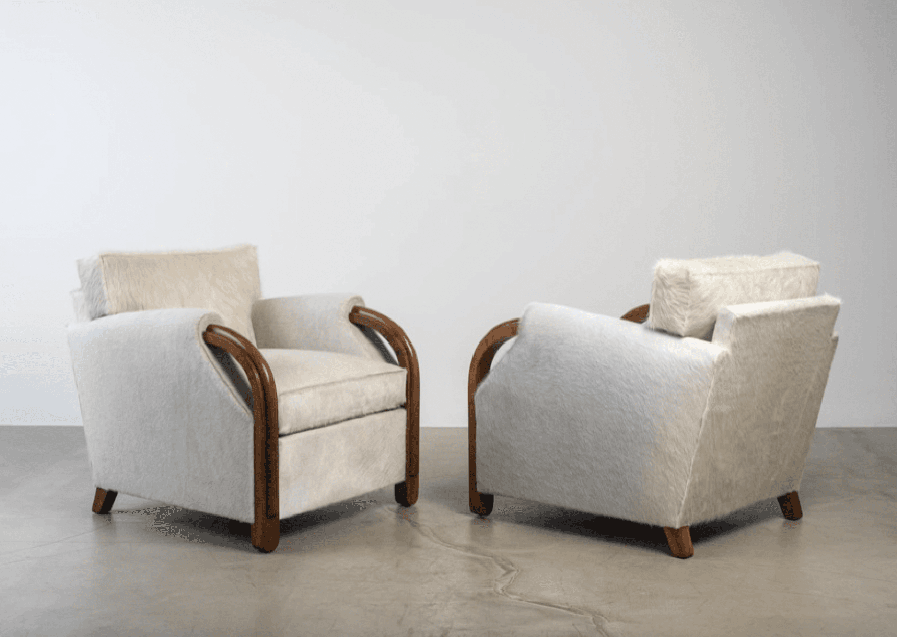 An Art Deco-inspired armchair featuring a plush hair-on-hide upholstery in an off-white or cream color, complemented by distinctive bentwood arms in a dark wood finish. The chair has a squared silhouette, a separate seat cushion, and a removable back cushion, all upholstered in the same material. Its design showcases elegant curves in the armrests contrasted with the rectilinear form of the body. — 3D model