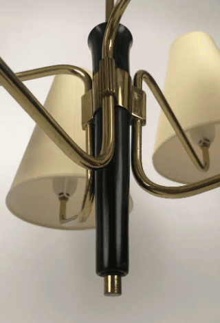 A vintage Mid-Century Modern chandelier featuring a central brass stem descending from a ceiling canopy. Six radiating arms, also in brass, extend outwards, each terminating in an upward-pointing, conical, off-white fabric shade. The central column has a prominent black accent piece, providing a striking contrast to the brass finish. The design is characteristic of the 1950s to 1960s, emphasizing clean lines and functional elegance. — 3D model