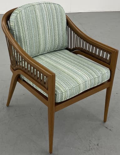 A barrel-back armchair featuring a warm-toned wooden frame, likely teak or oak, with distinctive woven or rope detailing along the arms and backrest. The chair is upholstered with removable seat and back cushions in a textured, multi-tonal green, white, and blue striped fabric. Its design combines elegant curves with a relaxed, tropical-modern aesthetic. — 3D model
